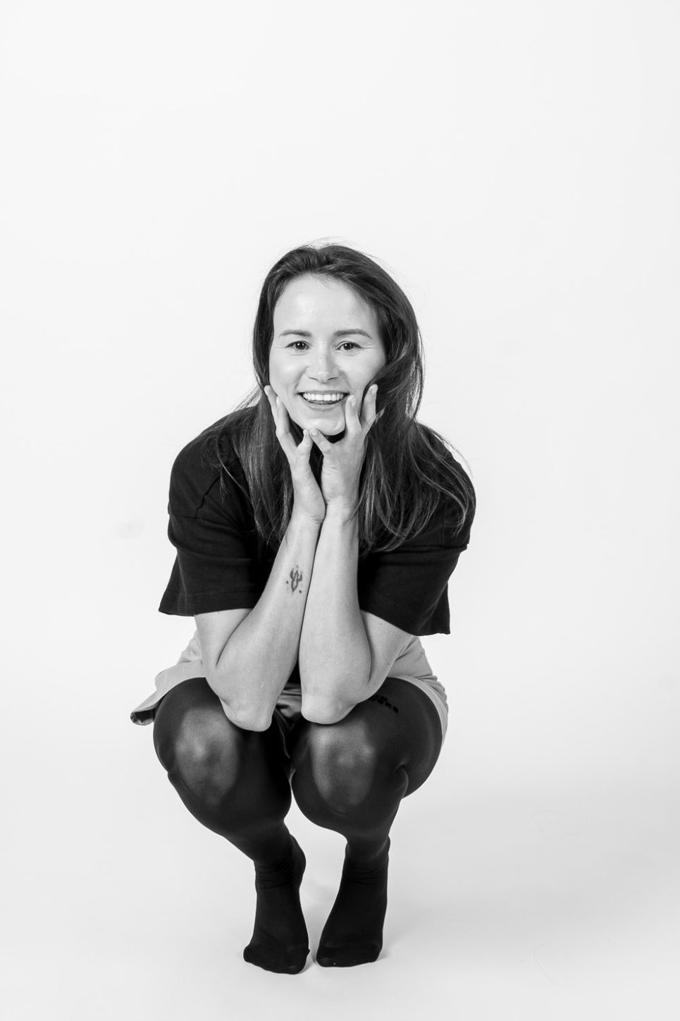 Frau hockt lachend auf weißem Hintergrund und fotografiert sich selbst