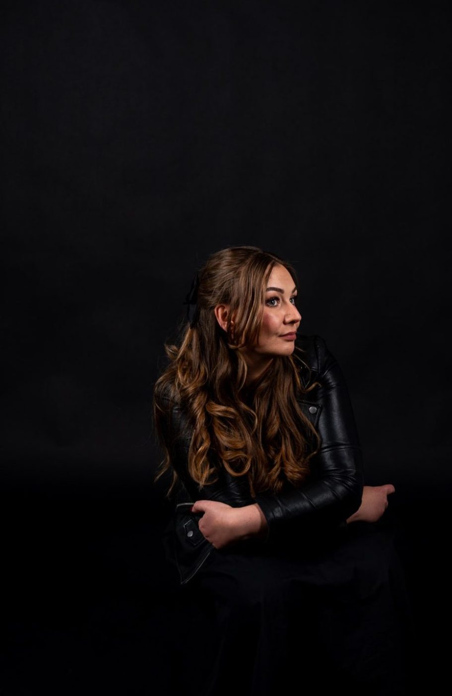 Frau mit Lederjacke sitzt vor schwarzem Hintergrund im AuraMirror Studio