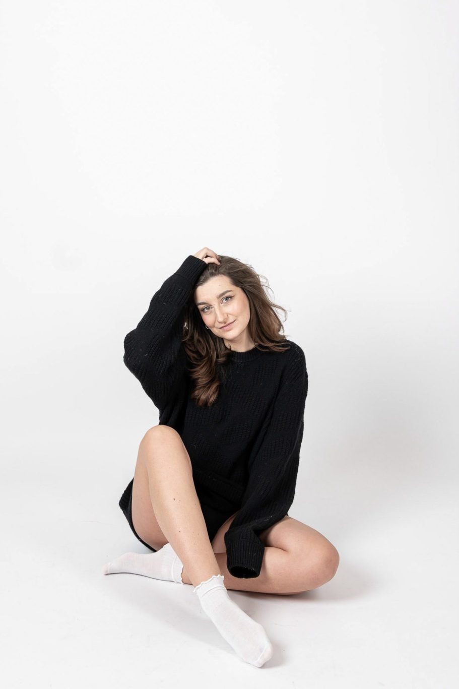 Frau im weißen Jumpsuit sitzt auf Stuhl vor schwarzem Hintergrund